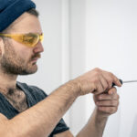 Man installing or repairing a ceiling light while holding electrical wires and using a screwdriver.