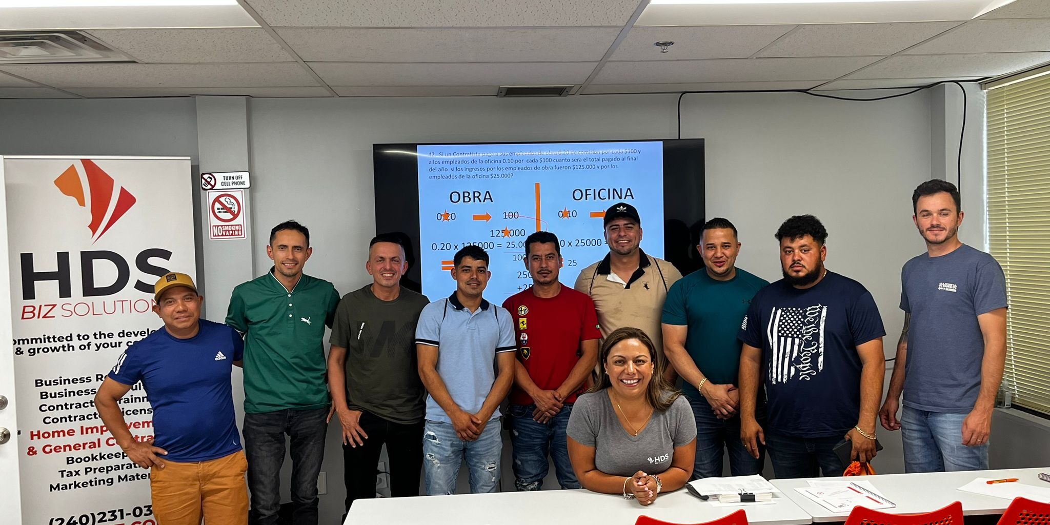 Participantes en una clase de HDS Biz Solutions sobre la licencia de contratista en Maryland, posando junto a la instructora frente a un aula, con una presentación en pantalla