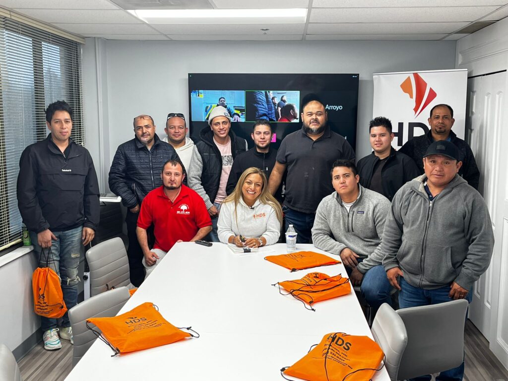 Participantes en una clase de HDS Biz Solutions sosteniendo certificados, sentados alrededor de una mesa de conferencias, participando en una capacitación sobre licencias de contratista.