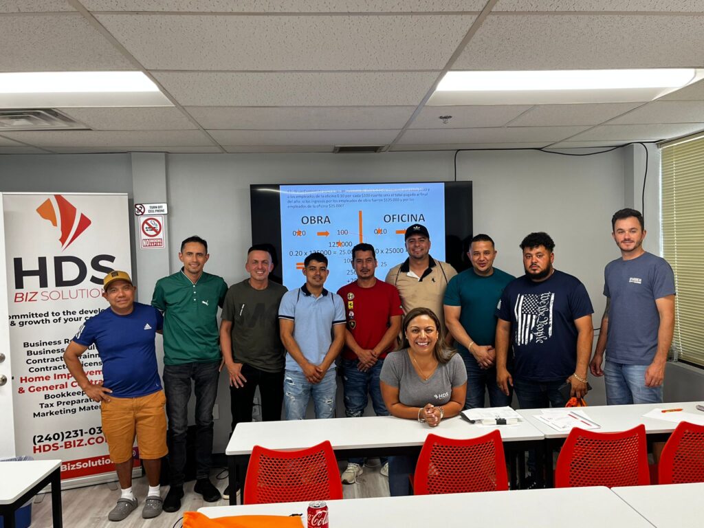 Participantes en una clase de HDS Biz Solutions sobre la licencia de contratista en Maryland, posando junto a la instructora frente a un aula, con una presentación en pantalla