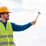 Trabajador de construcción con chaleco de seguridad y casco, sosteniendo un martillo al aire libre, representando profesionalismo y preparación en el sitio de trabajo