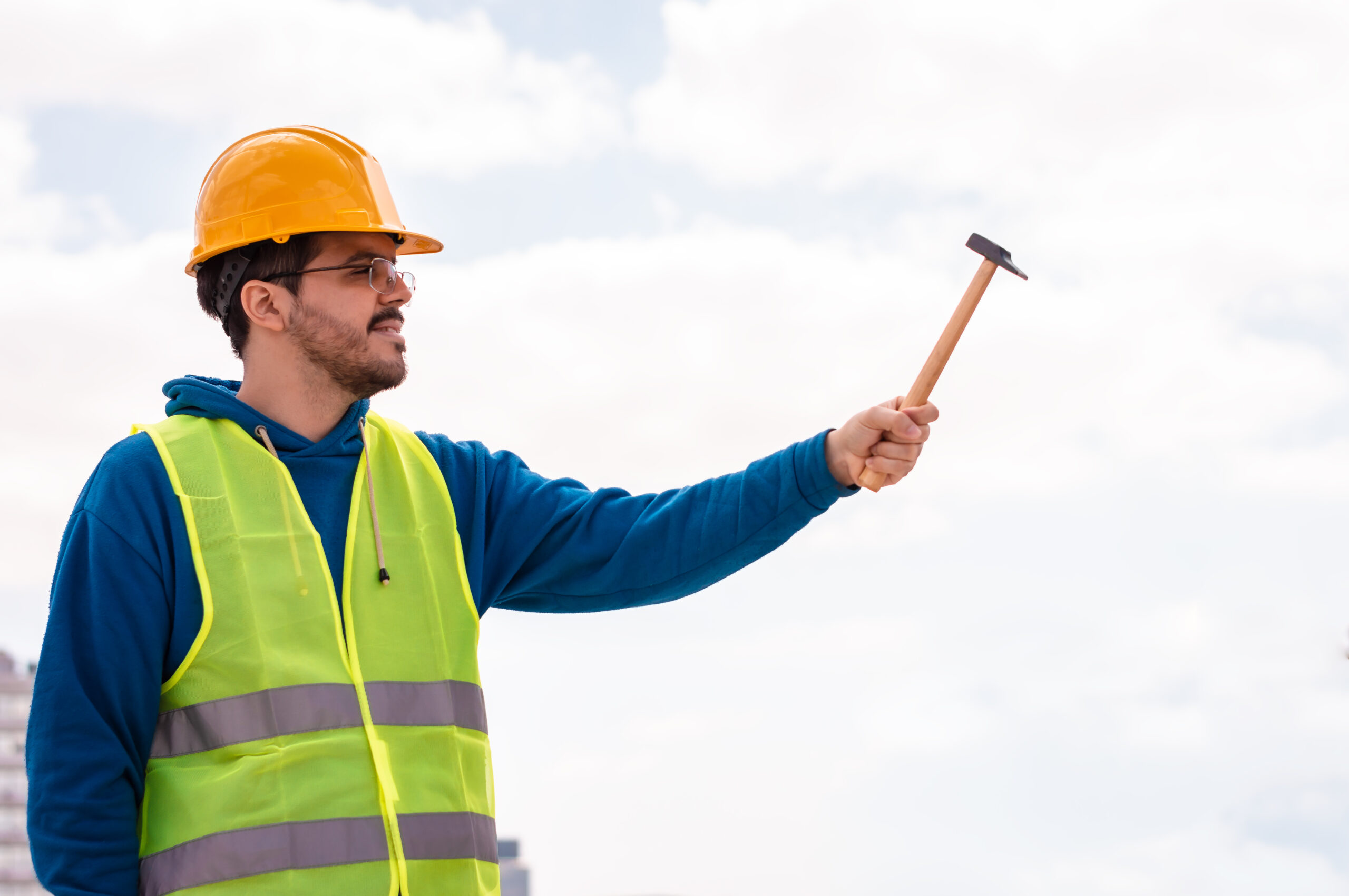 Trabajador de construcción con chaleco de seguridad y casco, sosteniendo un martillo al aire libre, representando profesionalismo y preparación en el sitio de trabajo