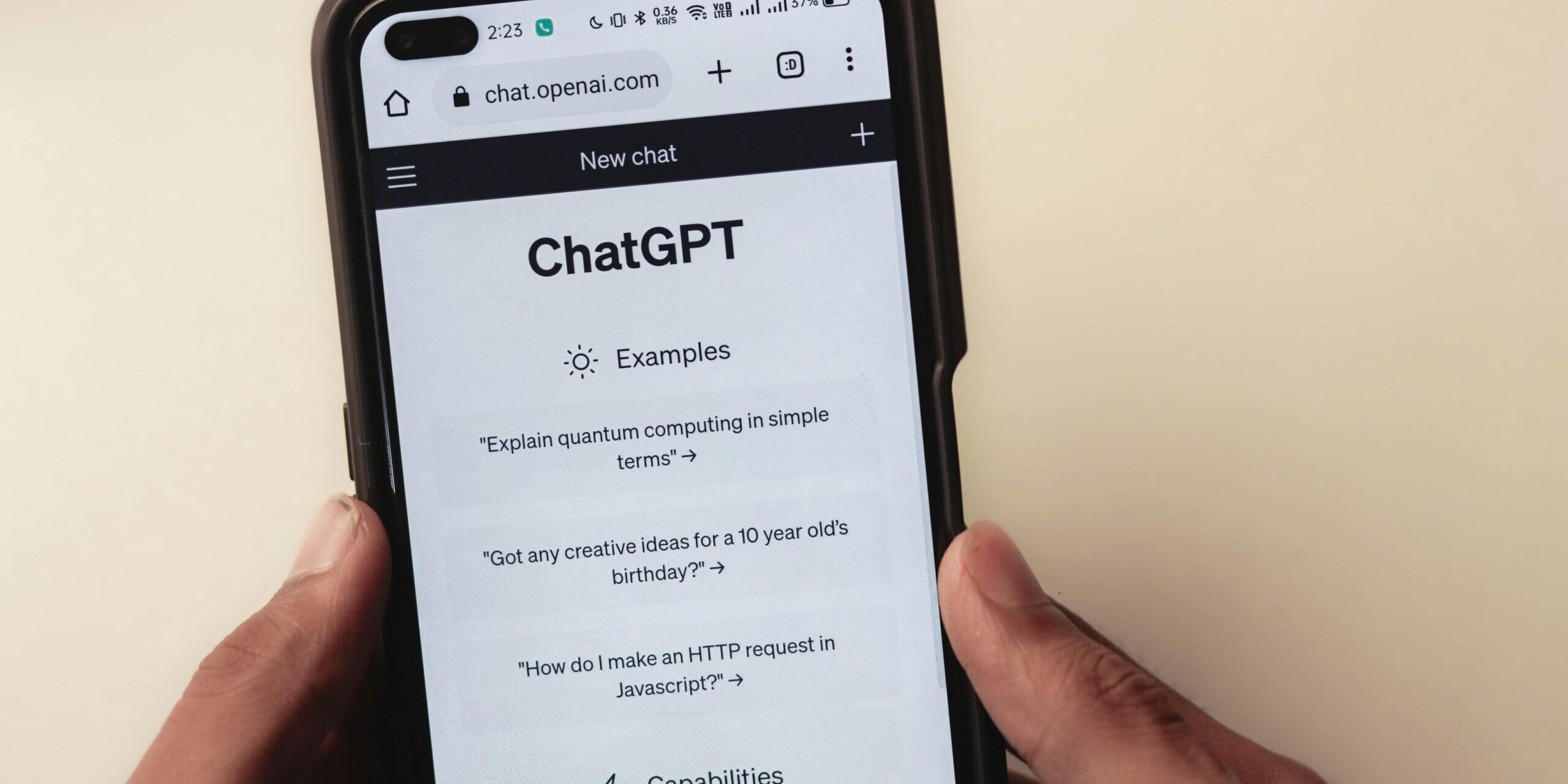 Persona sosteniendo un teléfono móvil que muestra la página de inicio de ChatGPT en el sitio web chat.openai.com, con ejemplos de preguntas visibles en la pantalla