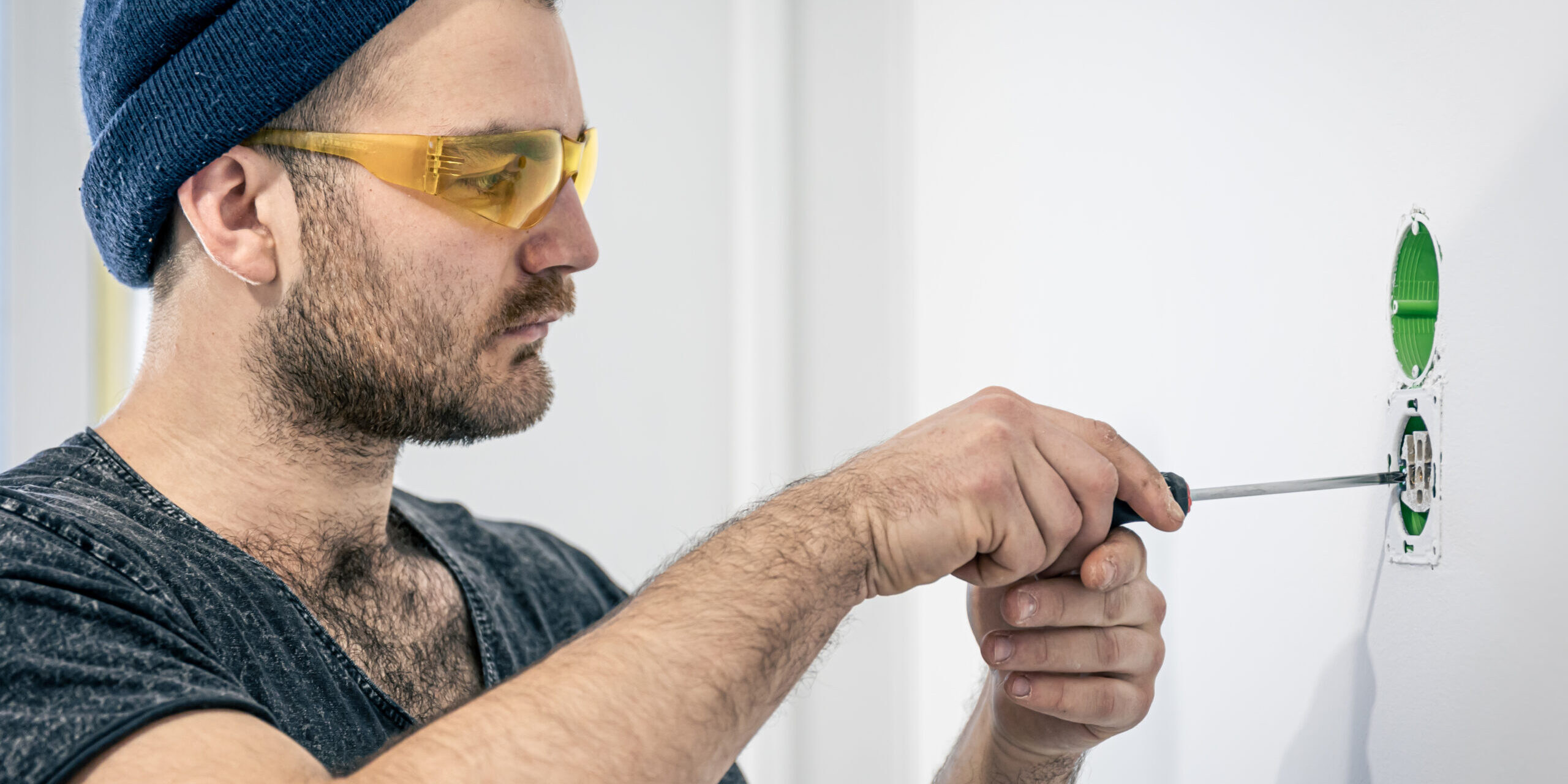 Man installing or repairing a ceiling light while holding electrical wires and using a screwdriver.