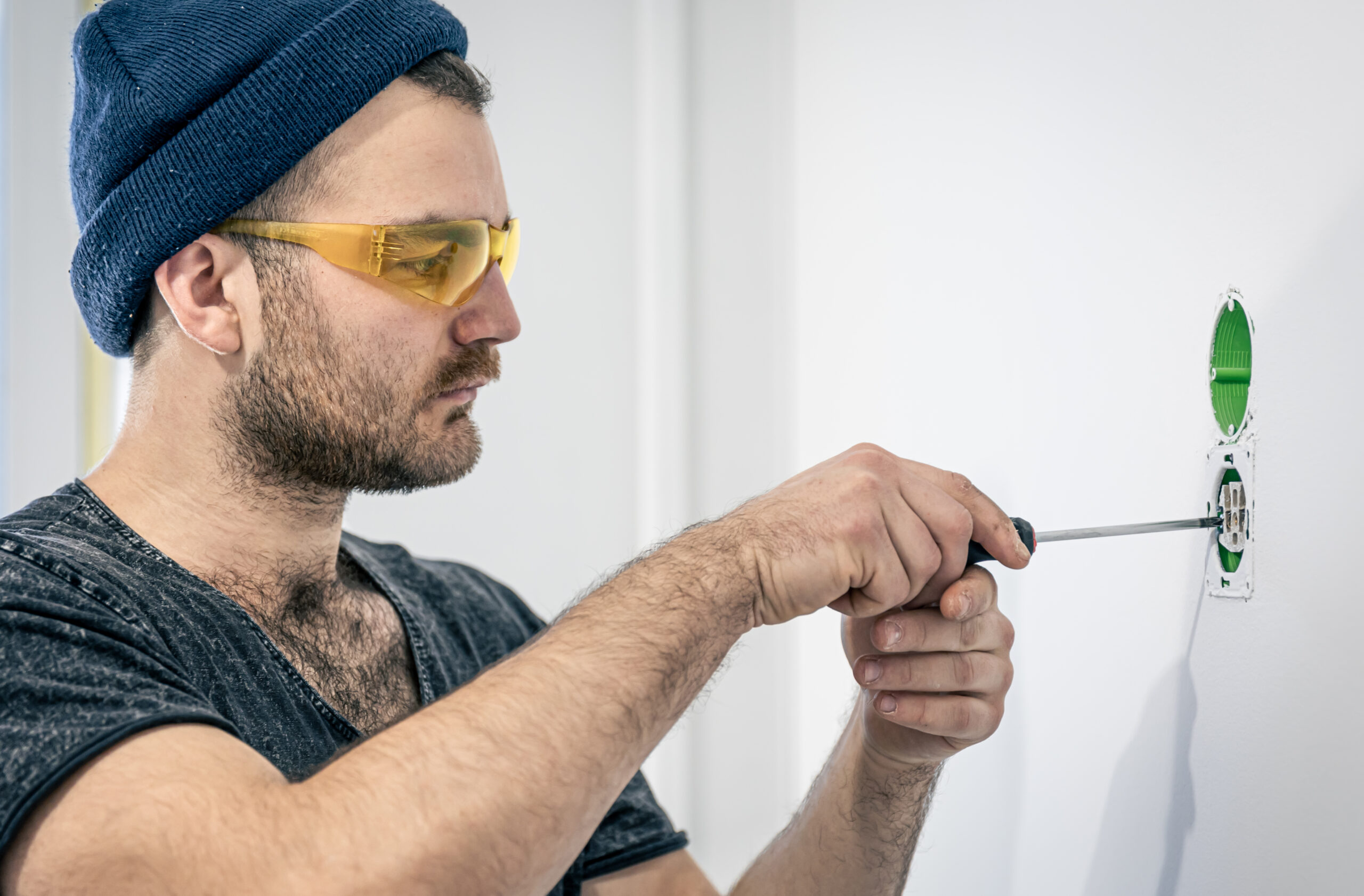 Man installing or repairing a ceiling light while holding electrical wires and using a screwdriver.