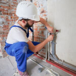 Hombre en casco de seguridad lubricando la tubería de agua para reducir la fricción y proporcionar una lubricación duradera. Hombre plomero en mono de trabajo instalando sistema de agua en el apartamento. Concepto de obras de fontanería