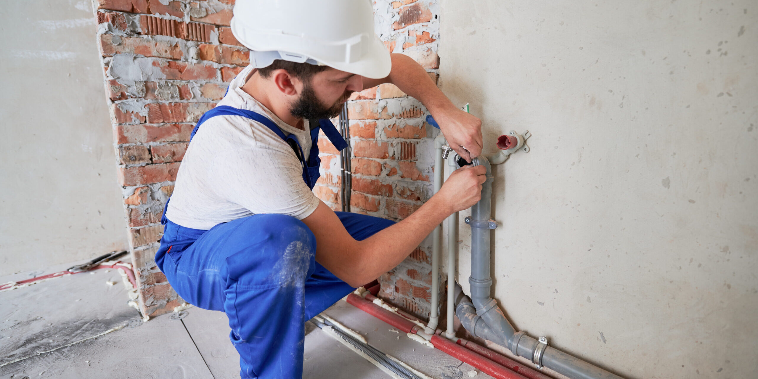 Hombre en casco de seguridad lubricando la tubería de agua para reducir la fricción y proporcionar una lubricación duradera. Hombre plomero en mono de trabajo instalando sistema de agua en el apartamento. Concepto de obras de fontanería