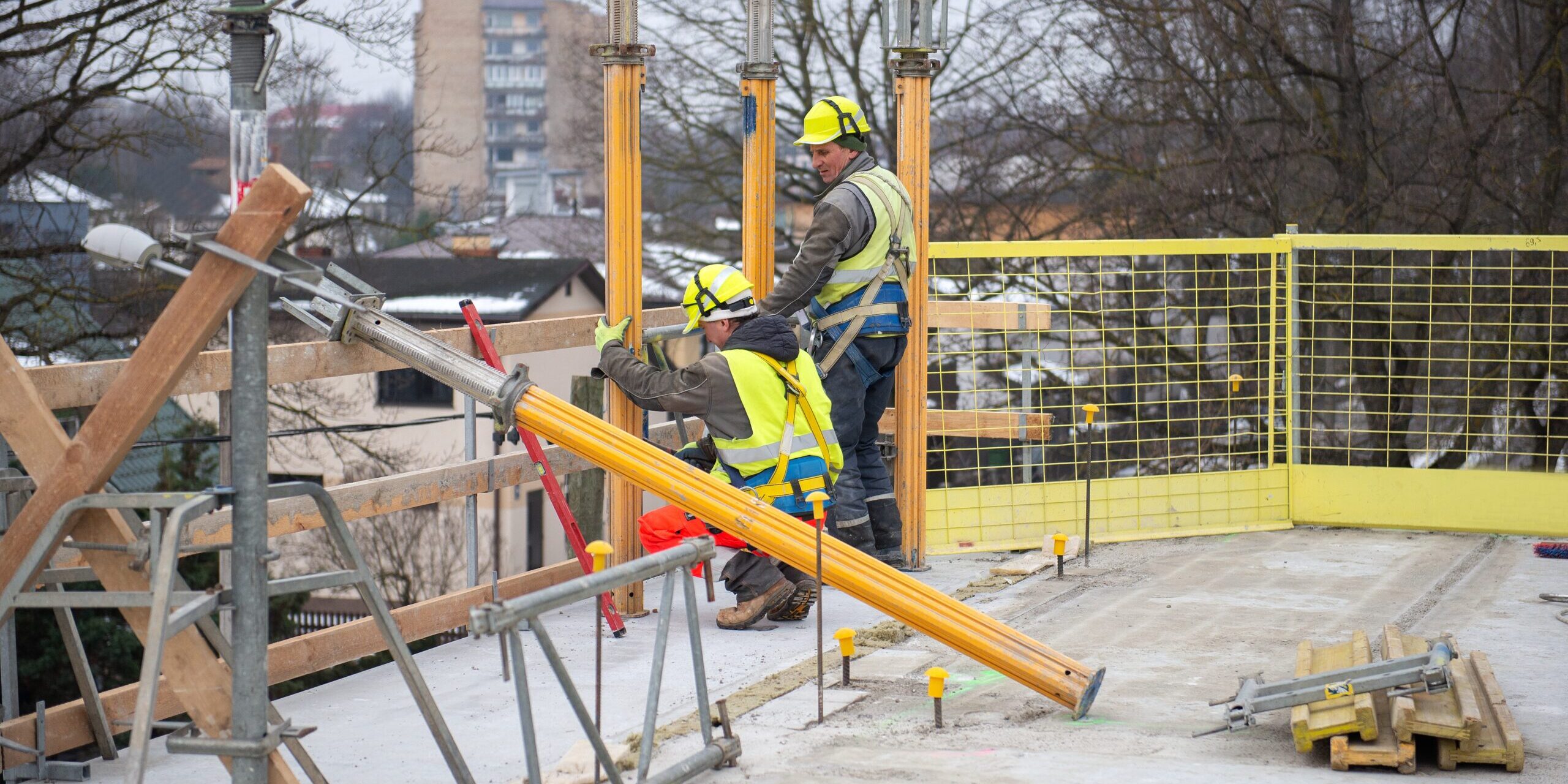 Dos trabajadores de la construcción en proceso de trabajo en el sitio de construcción con casco y chaleco de alta visibilidad