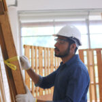Construction worker wearing a safety helmet and gloves while measuring and preparing wooden structures on a construction project in the United States