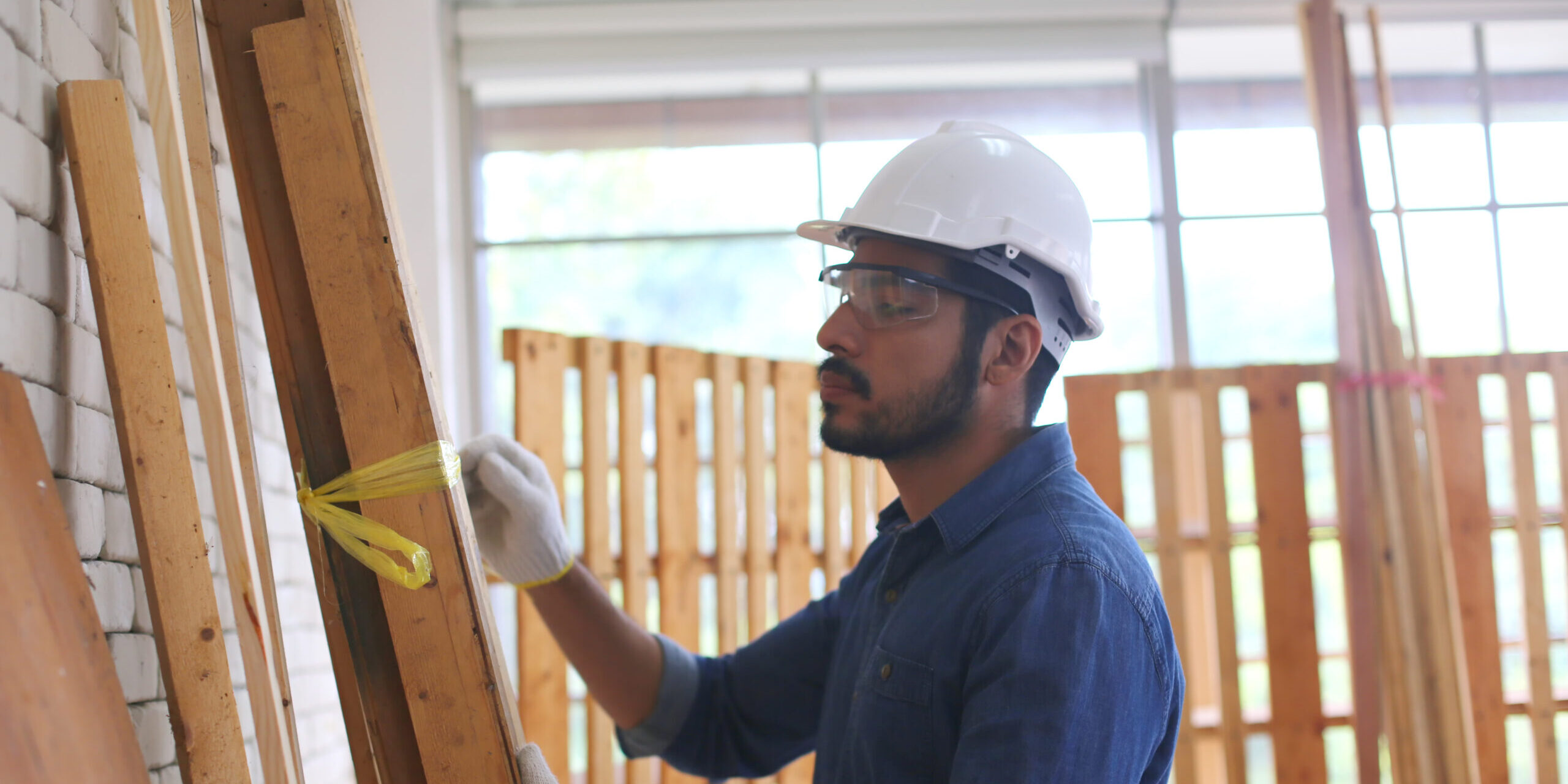 Construction worker wearing a safety helmet and gloves while measuring and preparing wooden structures on a construction project in the United States