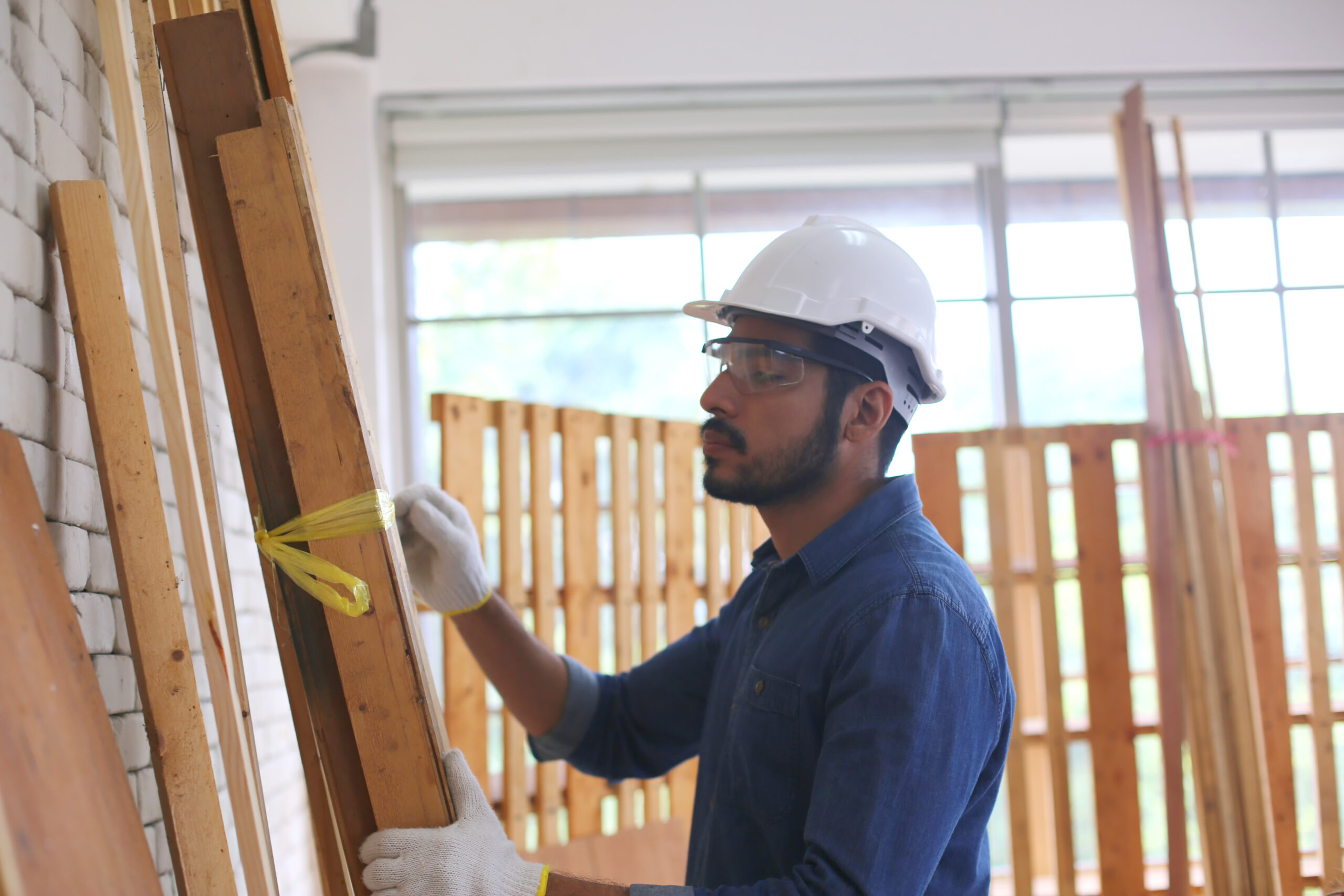 Construction worker wearing a safety helmet and gloves while measuring and preparing wooden structures on a construction project in the United States
