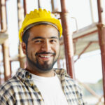 Smiling construction worker wearing a yellow safety helmet at a job site, representing a professional contractor in the United States.