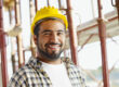 Smiling construction worker wearing a yellow safety helmet at a job site, representing a professional contractor in the United States.