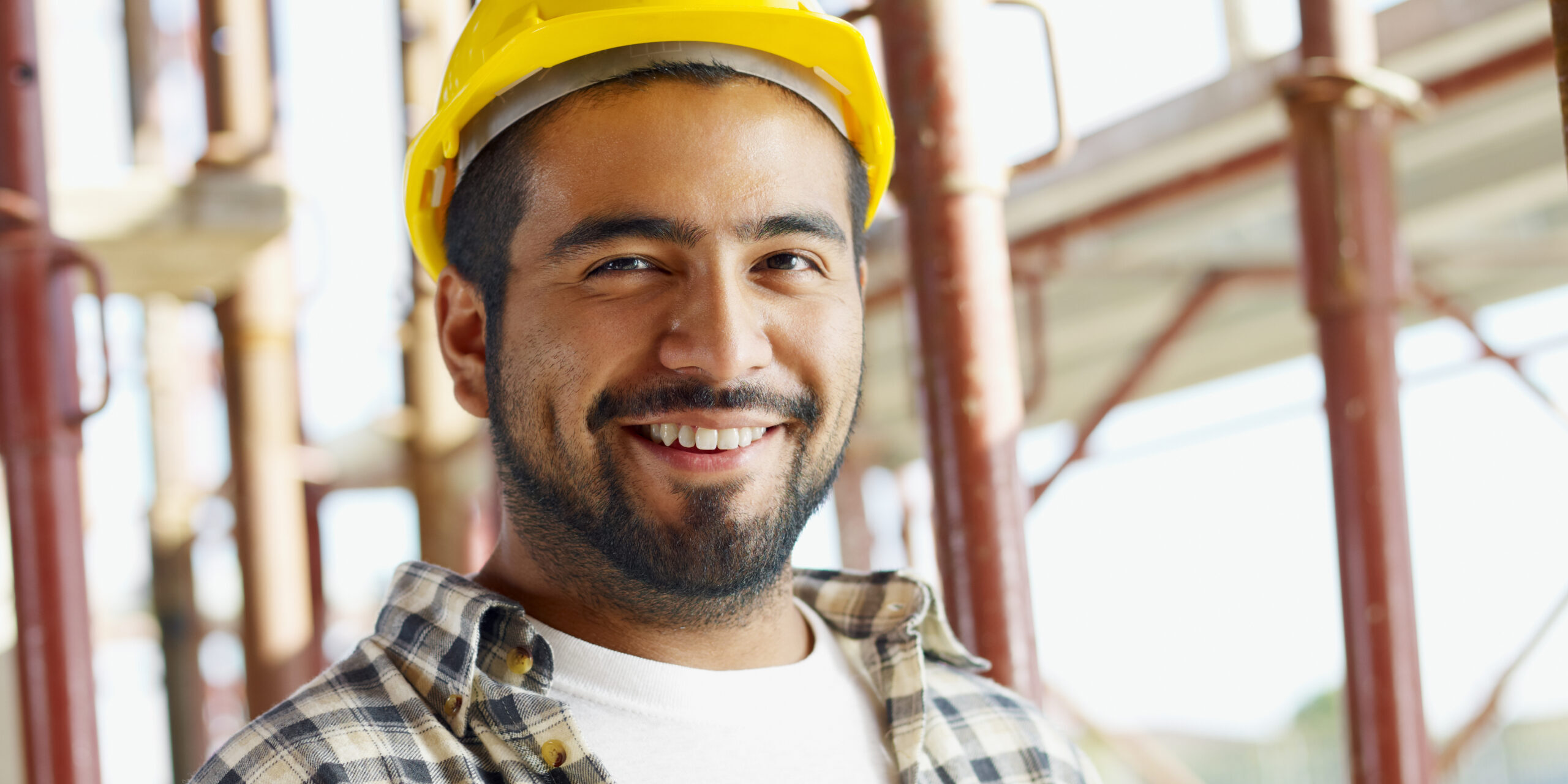 Smiling construction worker wearing a yellow safety helmet at a job site, representing a professional contractor in the United States.