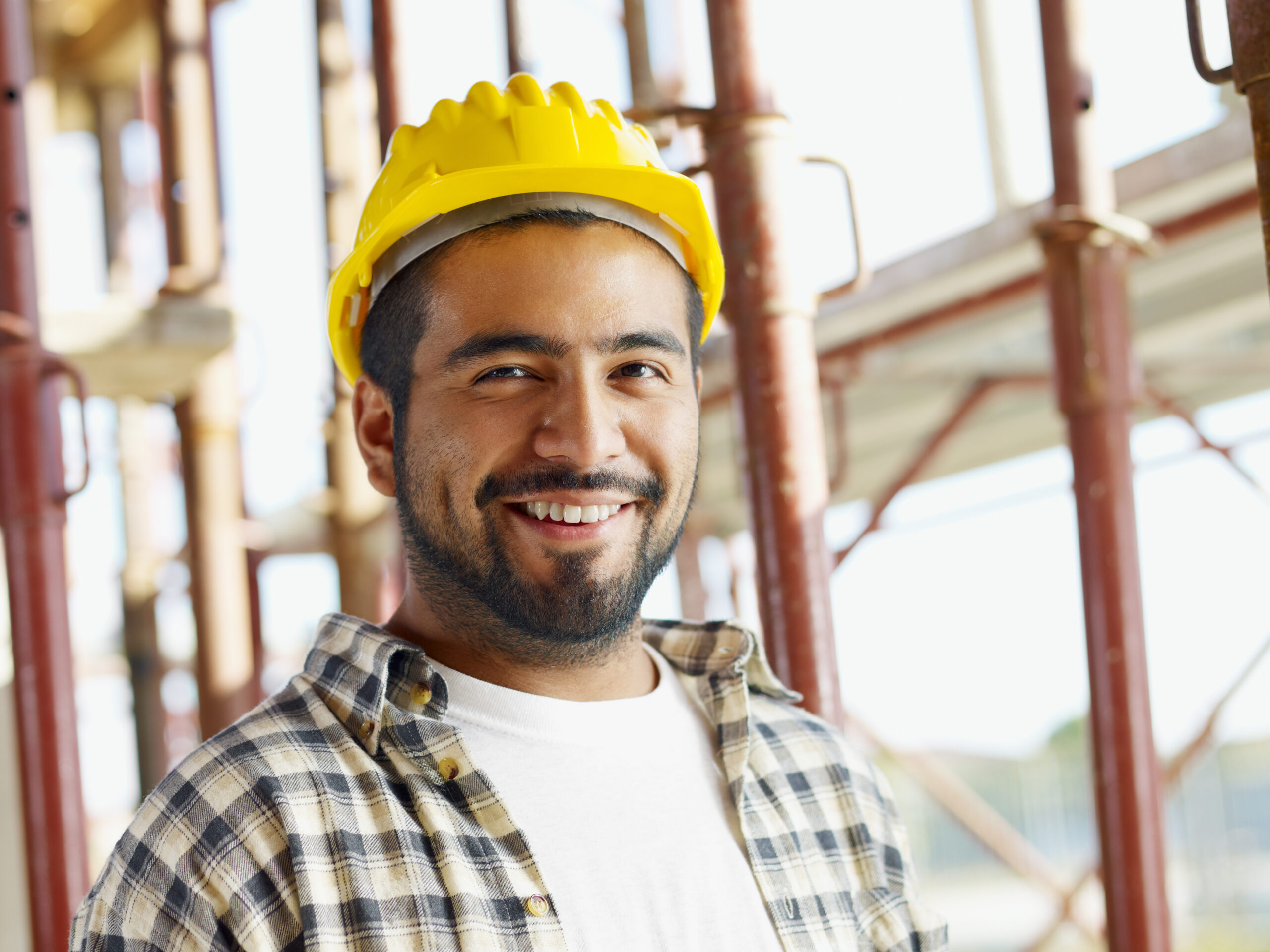 Smiling construction worker wearing a yellow safety helmet at a job site, representing a professional contractor in the United States.